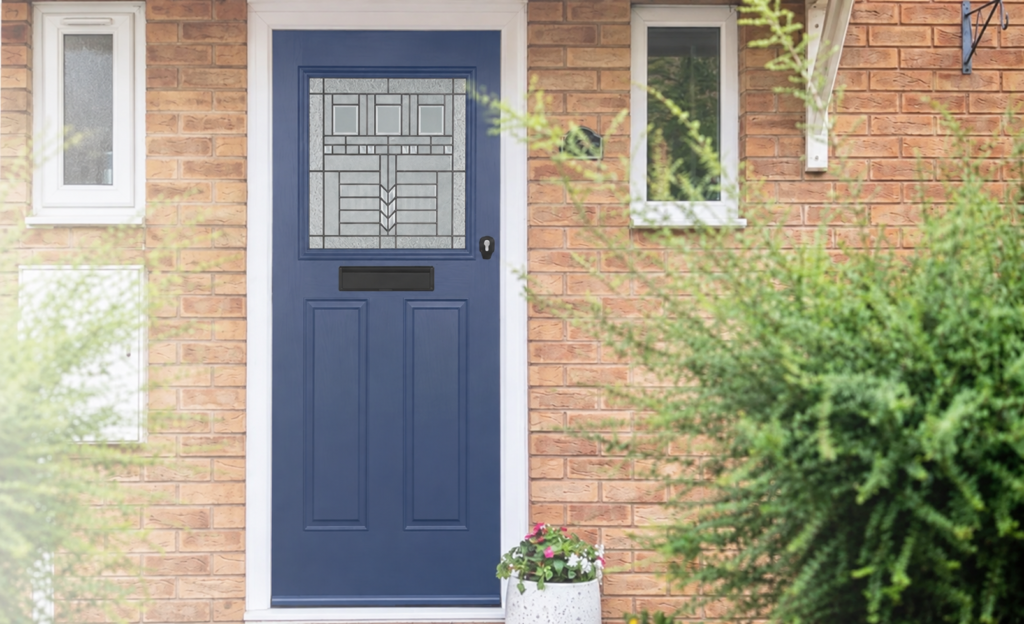 Navy blue front door with decorative glass panel set in a brick house, surrounded by greenery and a flower planter.